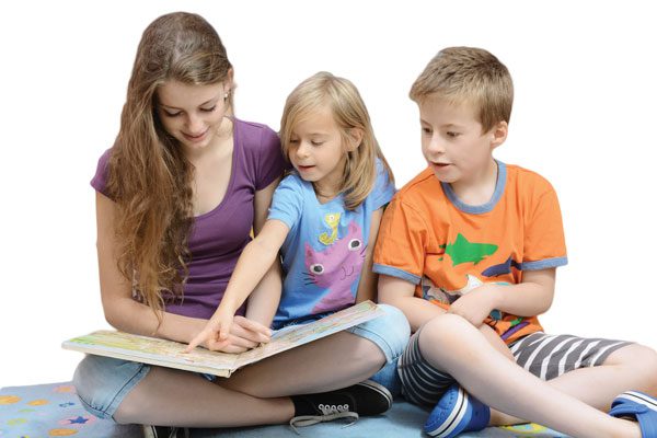 Girl babysitter looking at a book with two younger children